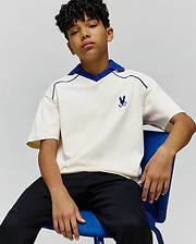 Kids Toby Jersey, a relaxed fit cream jersey polo with royal blue V-neck collar and piping, featuring a small embroidered blue Psycho Bunny skull logo on the left chest.