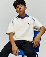 Kids Toby Jersey, a relaxed fit cream jersey polo with royal blue V-neck collar and piping, featuring a small embroidered blue Psycho Bunny skull logo on the left chest.