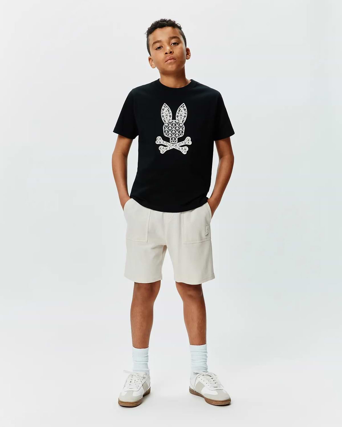 Black cotton jersey KIDS BRAD GRAPHIC TEE with a large, intricate white Psycho Bunny skull graphic on the chest, paired with cream relaxed-fit French terry shorts featuring a small embroidered logo.