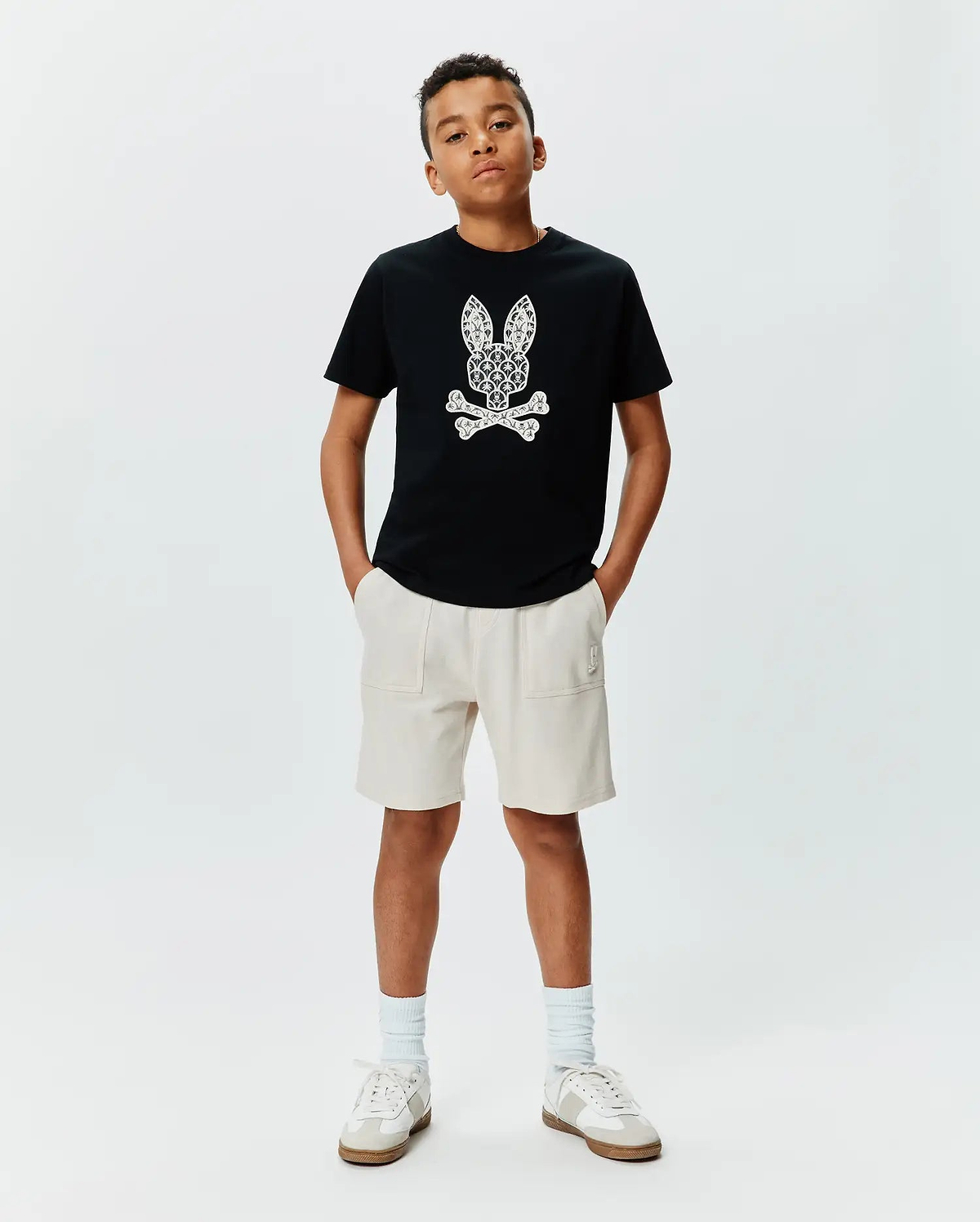 Black cotton jersey KIDS BRAD GRAPHIC TEE with a large, intricate white Psycho Bunny skull graphic on the chest, paired with cream relaxed-fit French terry shorts featuring a small embroidered logo.