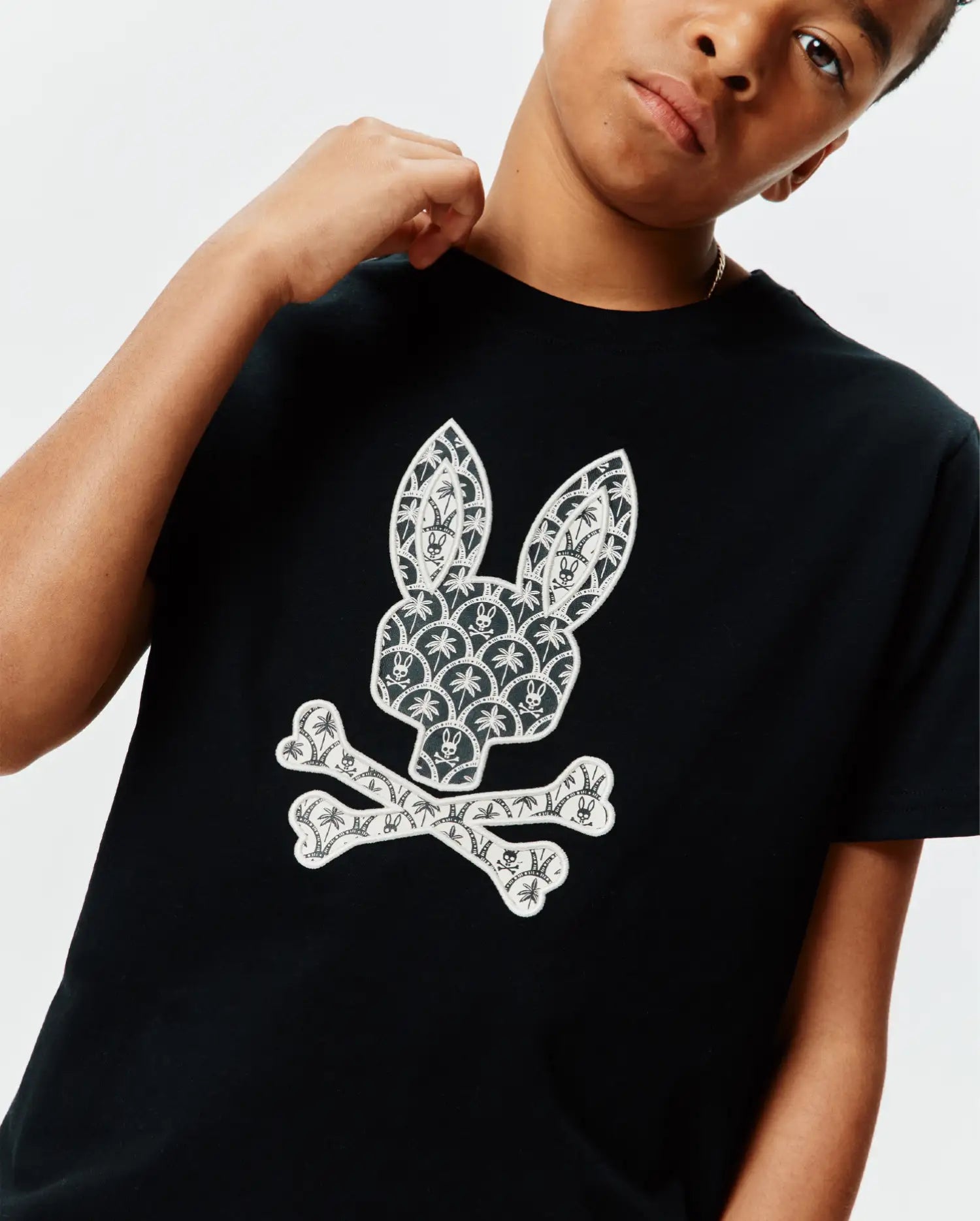 Black Kids Brad Graphic Tee, classic fit jersey, featuring a large white Psycho Bunny skull logo on the chest, intricately patterned with palm trees and mini bunny skulls.