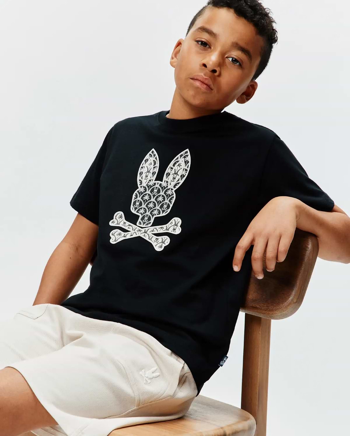 Kids Brad Graphic Tee, black cotton jersey, classic fit, featuring a large white Psycho Bunny skull and crossbones graphic with intricate palm tree and scale patterns, and a small blue hem tag.