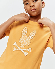 Kids Brad Graphic Tee in mustard yellow, featuring a large central Psycho Bunny skull and crossbones logo filled with a cream palm tree and mini bunny skull pattern, classic fit jersey knit.