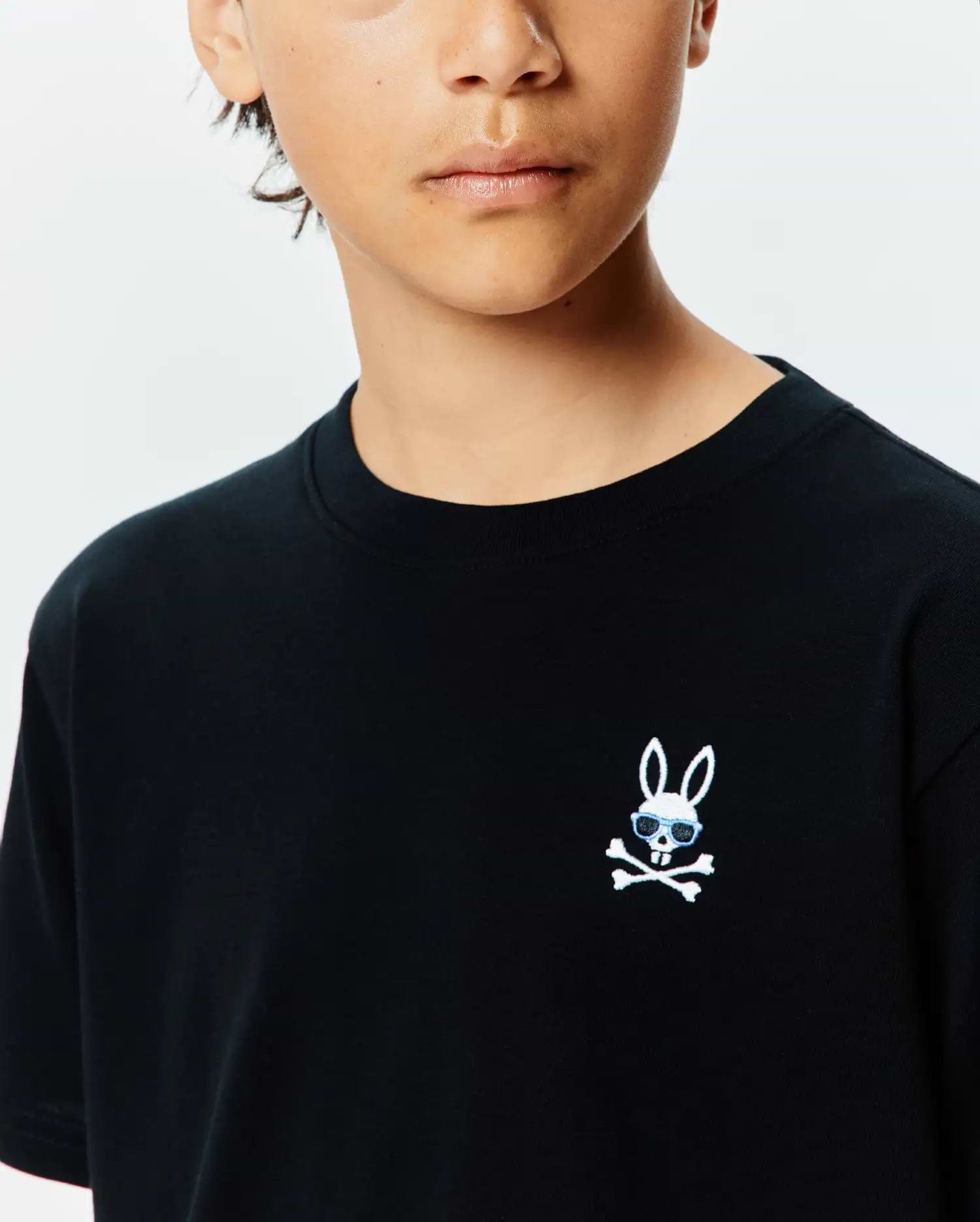 Kids Sunny Chest Graphic Tee, a black classic fit jersey t-shirt featuring a small embroidered white Psycho Bunny skull with light blue sunglasses and crossbones on the left chest.