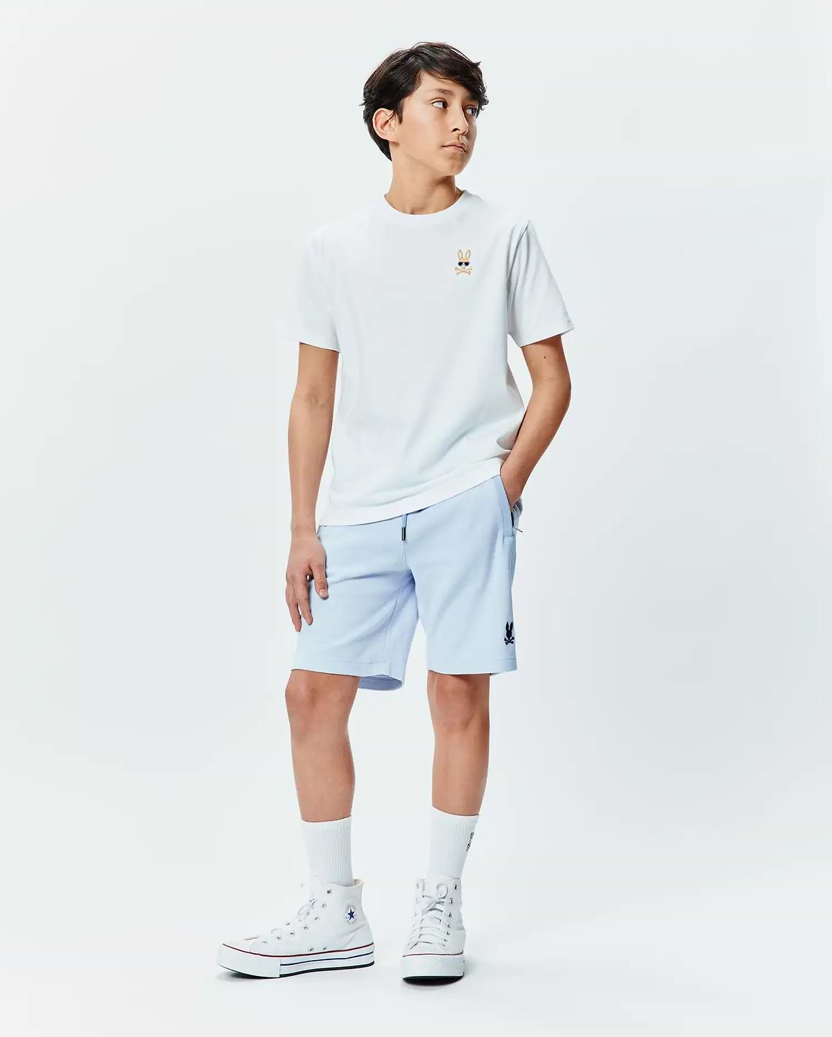 Kids Sunny Chest Graphic Tee, a white jersey t-shirt with a small embroidered Psycho Bunny skull in sunglasses on the chest. Light blue french terry shorts with a small Psycho Bunny logo on the thigh.