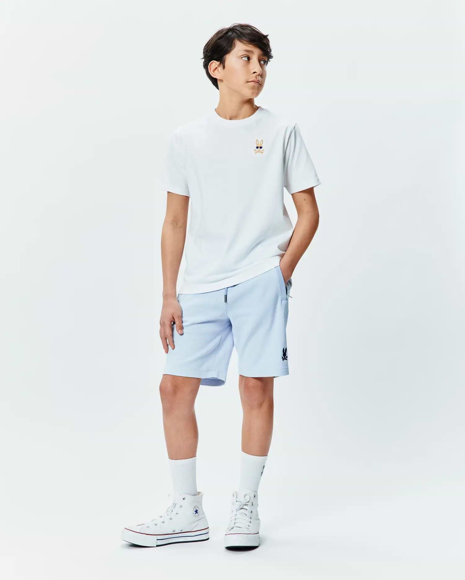 Kids Sunny Chest Graphic Tee, a white jersey t-shirt with a small embroidered Psycho Bunny skull in sunglasses on the chest. Light blue french terry shorts with a small Psycho Bunny logo on the thigh.