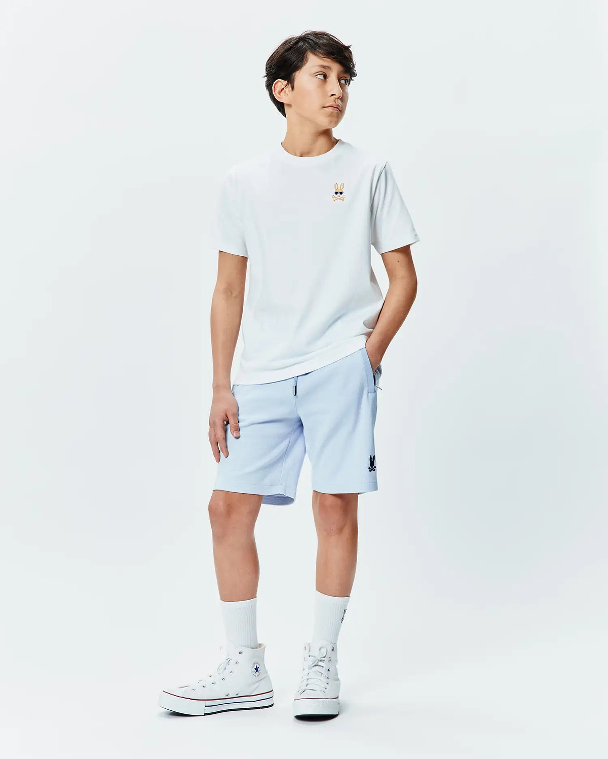 Kids Sunny Chest Graphic Tee, a white jersey t-shirt with a small embroidered Psycho Bunny skull in sunglasses on the chest. Light blue french terry shorts with a small Psycho Bunny logo on the thigh.