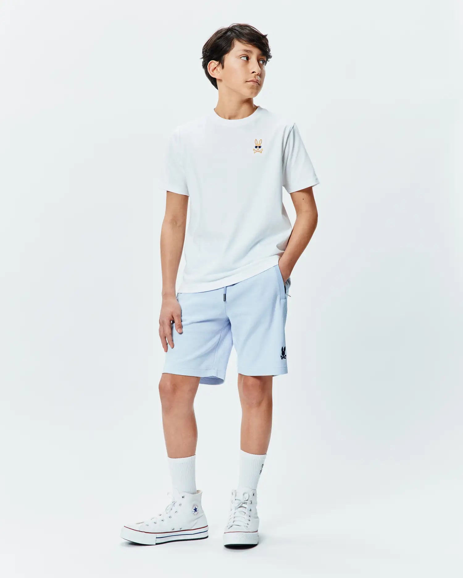 Kids Sunny Chest Graphic Tee, a white jersey t-shirt with a small embroidered Psycho Bunny skull in sunglasses on the chest. Light blue french terry shorts with a small Psycho Bunny logo on the thigh.