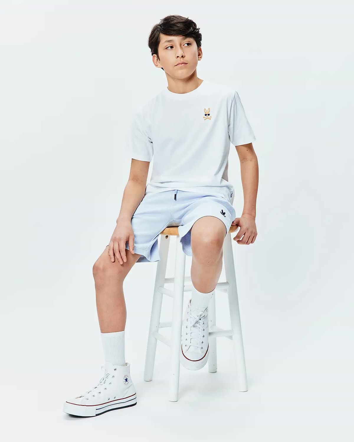 Kids Sunny Chest Graphic Tee, a white jersey t-shirt with a small embroidered Psycho Bunny skull in sunglasses on the left chest, paired with light blue relaxed-fit shorts featuring a small embroidered bunny logo on the right thigh.
