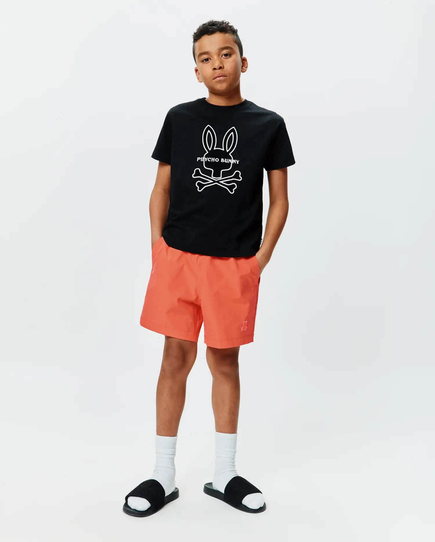 Kids Craig Graphic Tee in black jersey, classic fit, featuring a large white Psycho Bunny skull graphic on the chest, paired with coral woven shorts with a small embroidered Psycho Bunny logo on the left leg. (4)