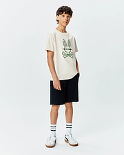 Kids Craig Graphic Tee, a classic fit cream jersey t-shirt with short sleeves, showcasing a prominent dark green outlined Psycho Bunny skull logo and text centered on the chest. (5)