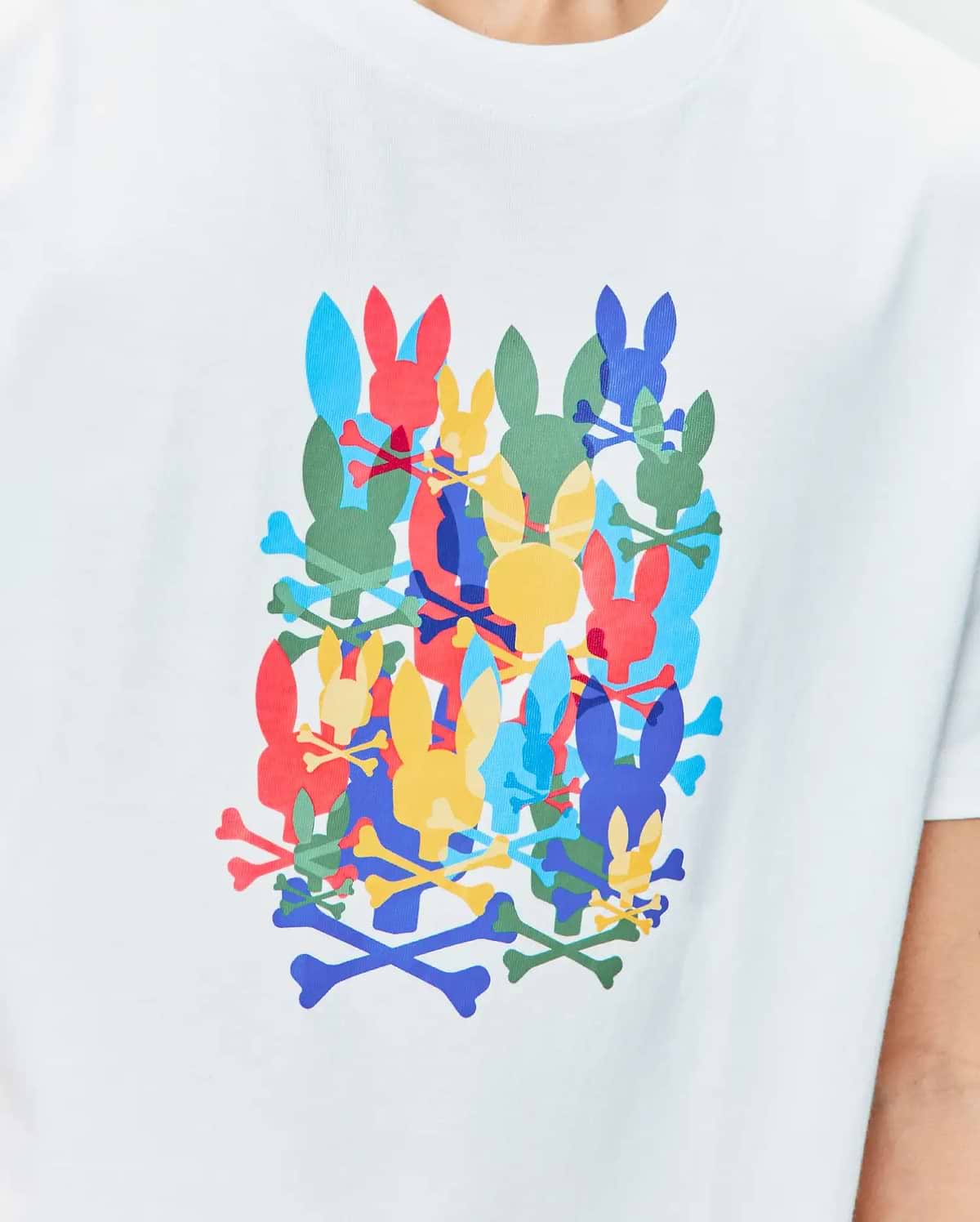 Kids Tanner Graphic Tee, a white classic fit jersey t-shirt featuring a large central graphic print of overlapping Psycho Bunny skull logos and crossbones in red, blue, yellow, green, and light blue.
