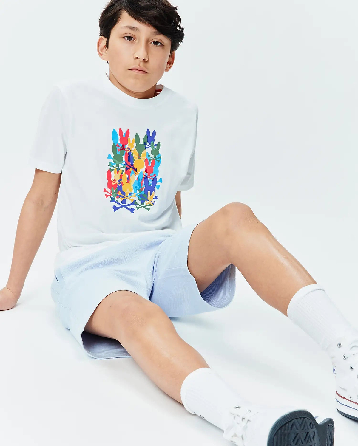 White Kids Tanner Graphic Tee with a large, vibrant stacked Psycho Bunny skull and crossbones print on the chest, paired with light blue textured pique shorts. Classic fit.