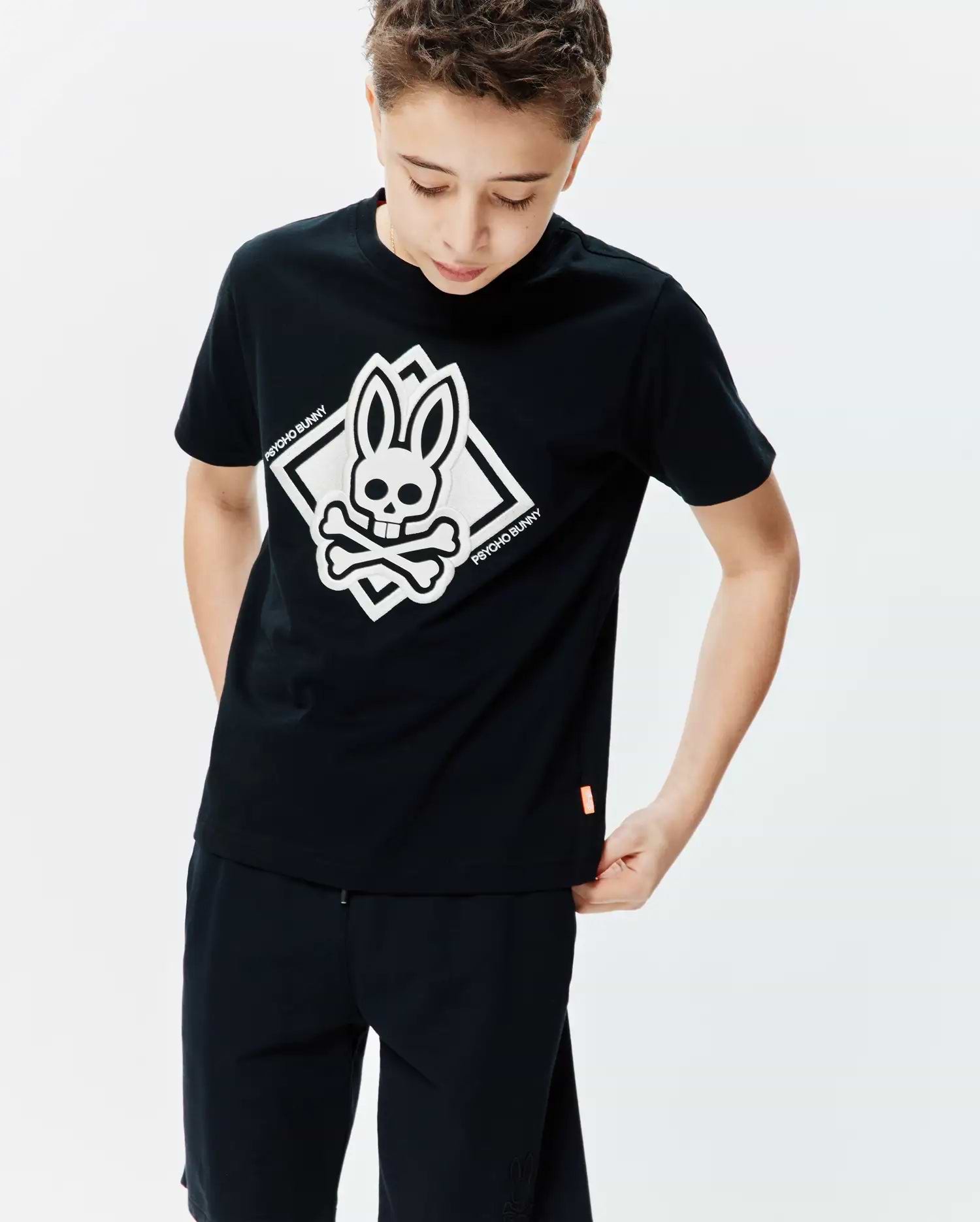 Black Kids Tobias Graphic Tee, a classic fit jersey t-shirt featuring a large white Psycho Bunny skull and crossbones graphic on the chest, outlined by a diamond, with a small orange hem tag.
