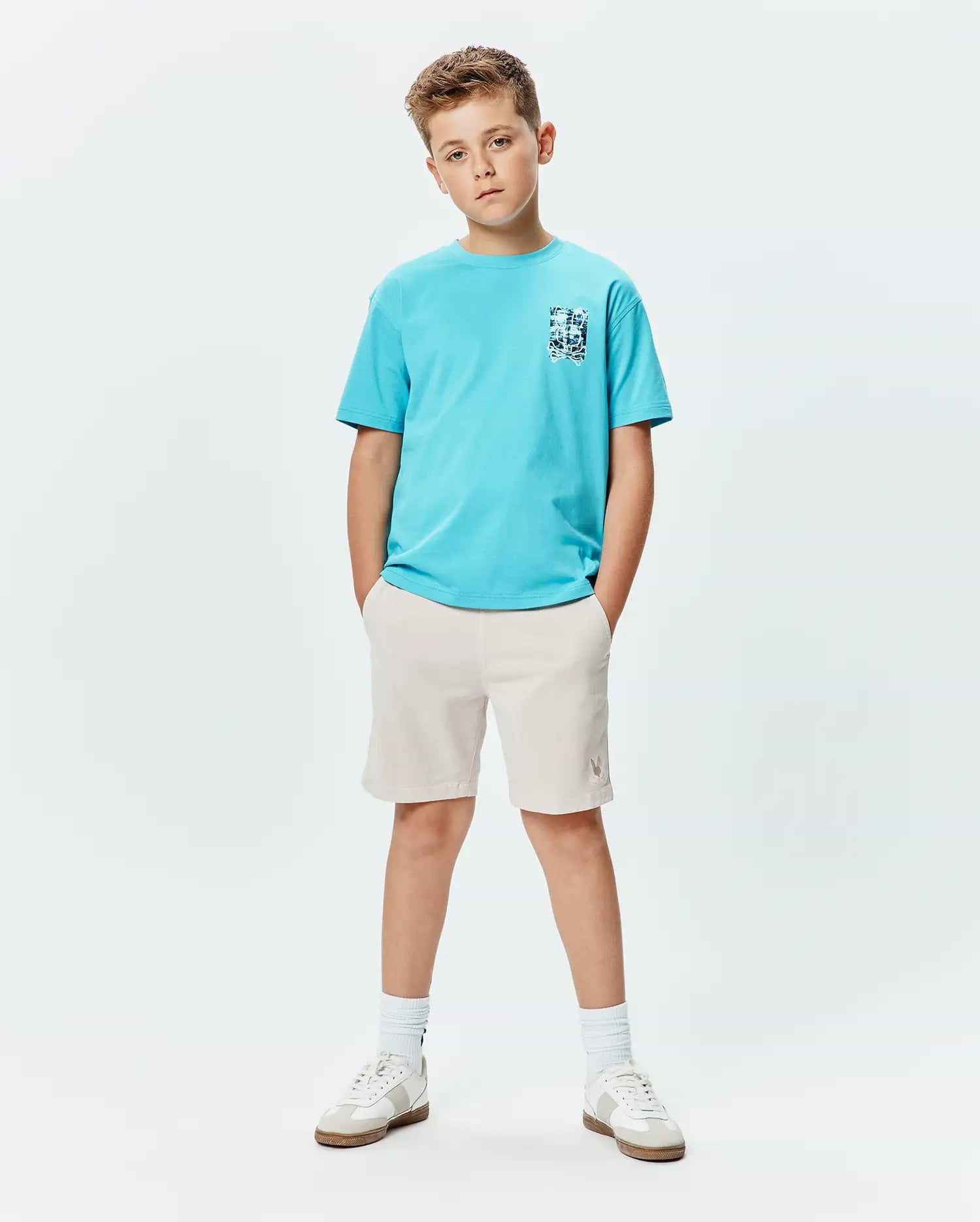 Kids Isaac Relaxed Fit Tee in bright blue jersey with a blue and white abstract bunny skull chest graphic, paired with light beige shorts featuring a small embroidered Psycho Bunny logo on the left thigh.