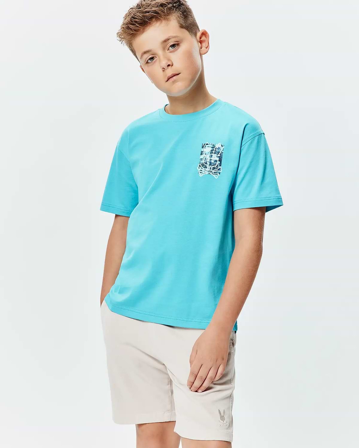 Kids Isaac Relaxed Fit Tee, an aqua blue jersey t-shirt with a relaxed fit and a small, distressed blue and white Psycho Bunny skull graphic on the left chest.