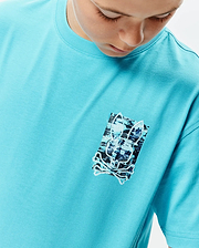 Kids Isaac Relaxed Fit Tee in vibrant turquoise jersey, featuring a relaxed fit and a distressed, pixelated Psycho Bunny skull graphic print on the left chest with black, white, and blue accents.