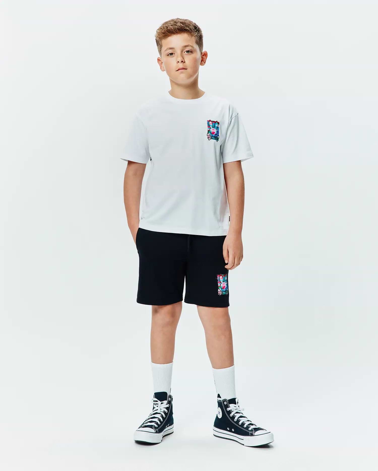 Kids Isaac Relaxed Fit Tee in white jersey with a small, colorful abstract bunny skull logo on the left chest, paired with black french terry shorts featuring a larger matching logo.