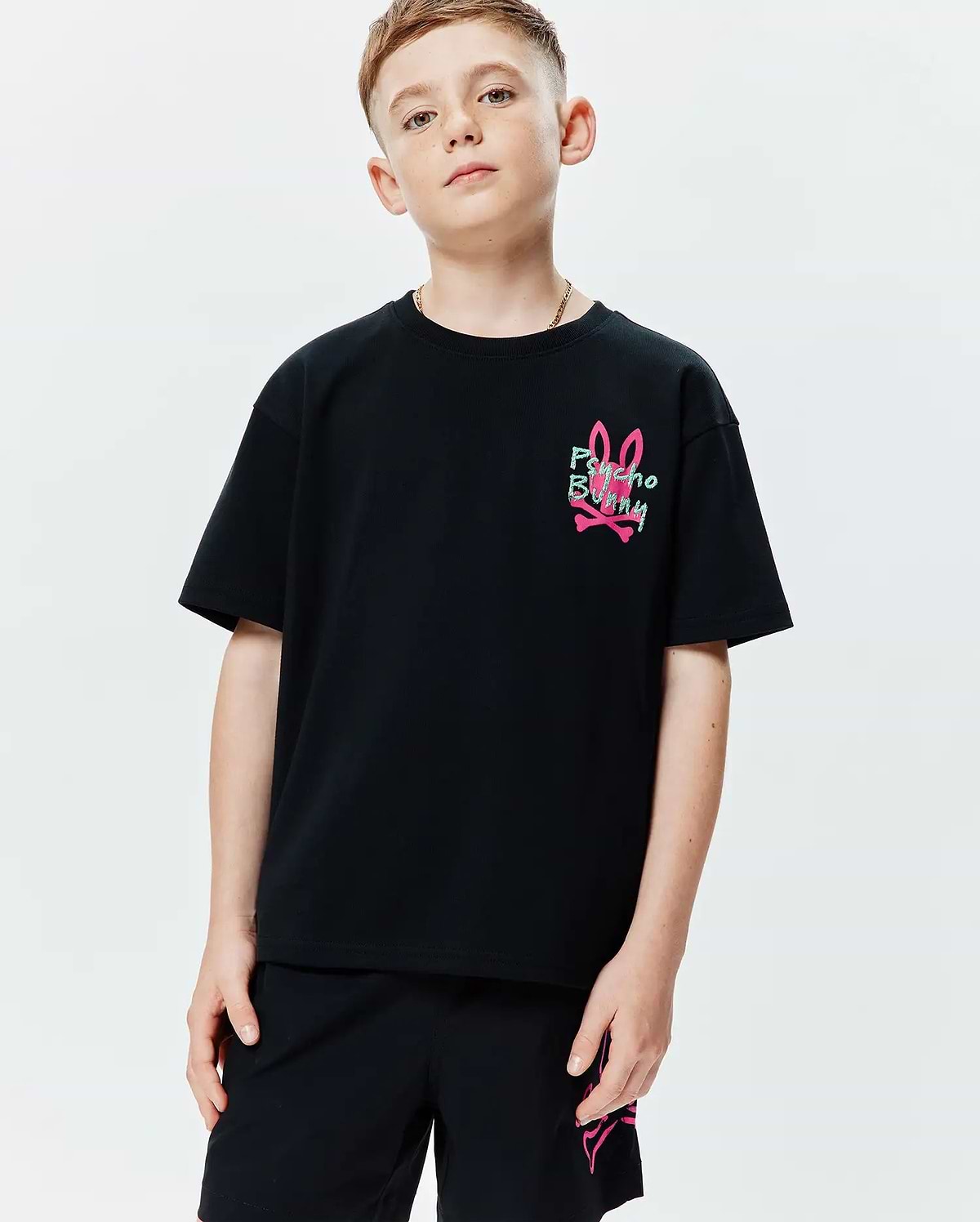 Kids Duncan Relaxed Fit Tee in black jersey knit, featuring a small graphic print of the pink bunny skull logo with green Psycho Bunny text on the left chest.