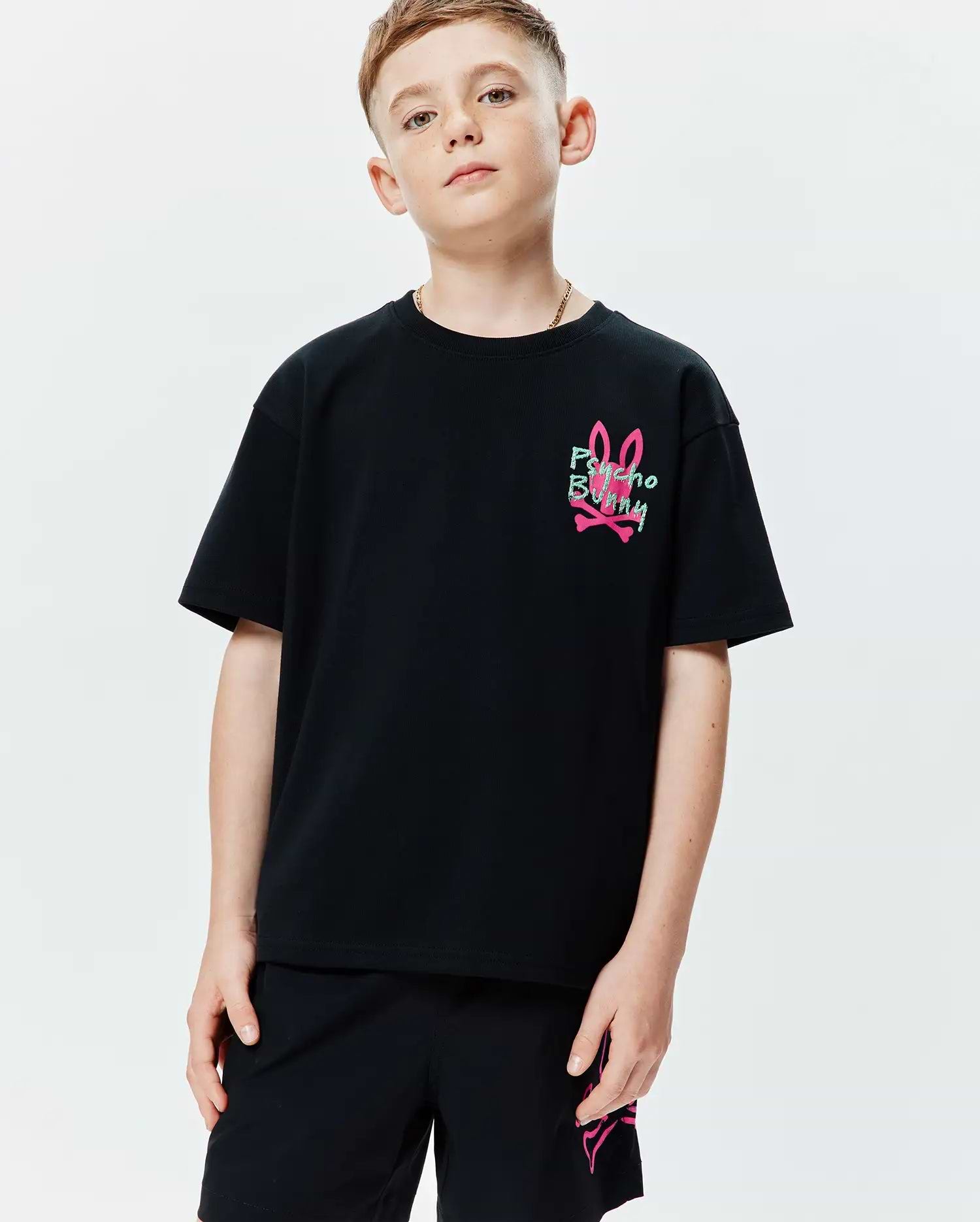 Kids Duncan Relaxed Fit Tee in black jersey knit, featuring a small graphic print of the pink bunny skull logo with green Psycho Bunny text on the left chest.