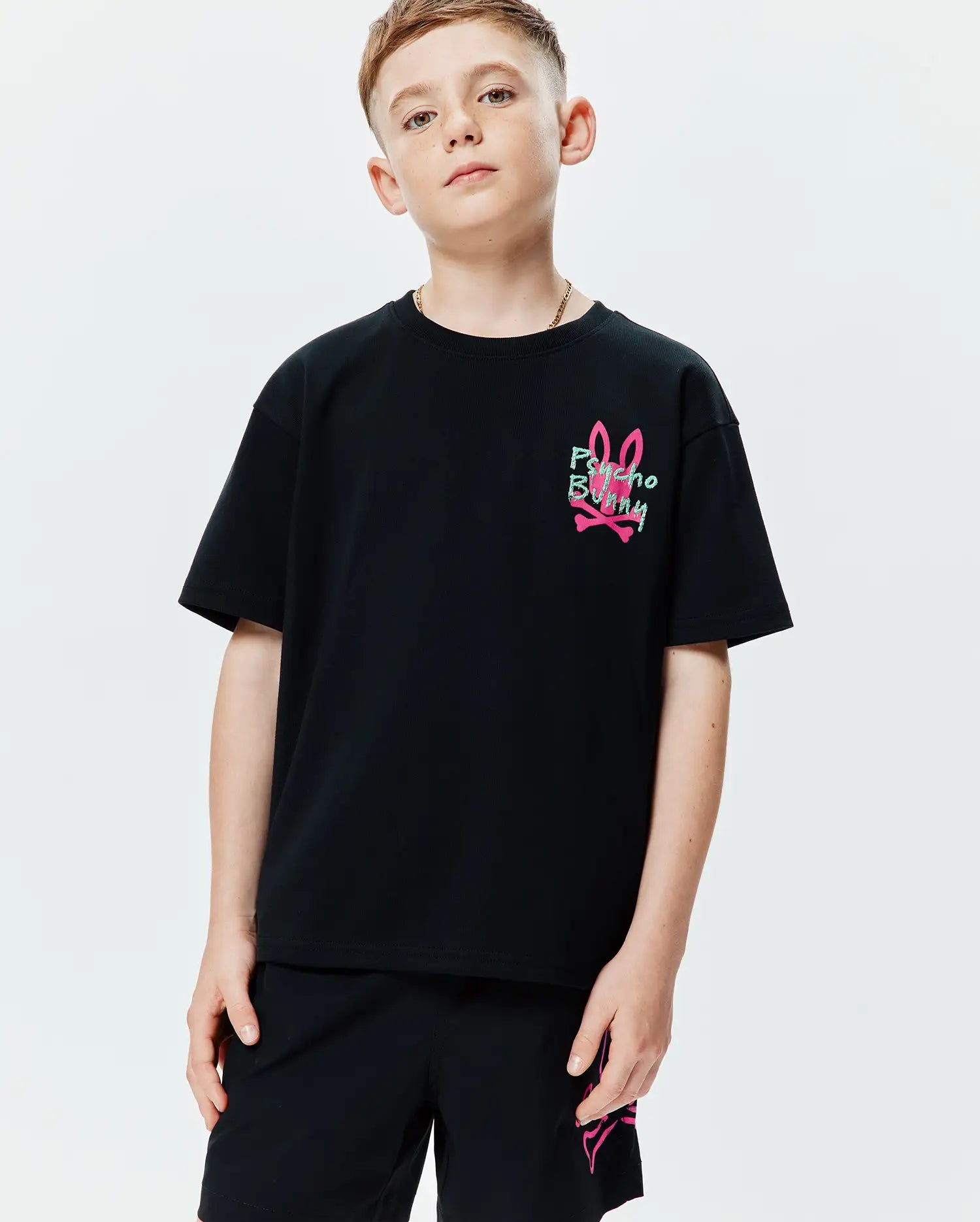 Kids Duncan Relaxed Fit Tee in black jersey knit, featuring a small graphic print of the pink bunny skull logo with green Psycho Bunny text on the left chest.