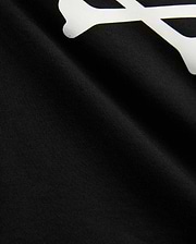 Kids Sunny Graphic Tee in black jersey knit, showcasing a large white graphic print of a bone, a key element of the iconic Psycho Bunny skull and crossbones logo.