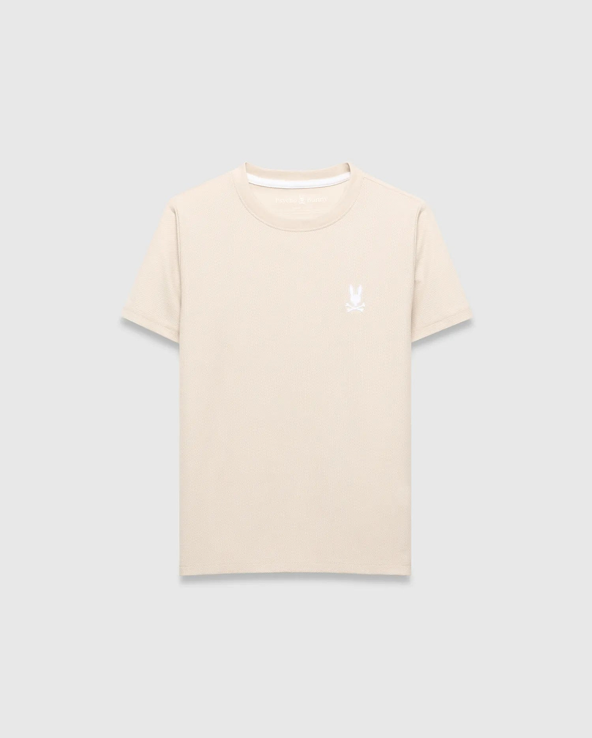 Kids Taylor Pique Tee in light beige, featuring a classic fit and pique fabric texture. It has a small, embroidered white Psycho Bunny skull logo on the left chest and a white accent trim on the collar.