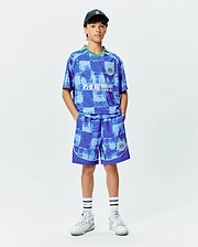 KIDS MICAH OVERSIZED SOCCER JERSEY and matching shorts in a blue distressed checkered pattern. Features a green V-neck, white PSYCHO BUNNY chest graphic, and circular crest logos. White piping details.