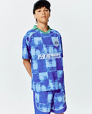 Kids Micah Oversized Soccer Jersey and matching shorts in a blue distressed checkerboard pattern with a green collar, white piping, a small Psycho Bunny Football Club crest, and a large PSYCHO BUNNY graphic on the chest.