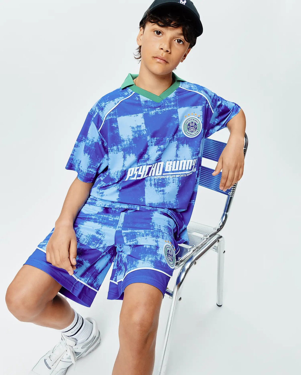 Kids Micah Oversized Soccer Jersey and shorts set, blue distressed checkered pattern. Green collar, white piping, embroidered Psycho Bunny Football Club crest on chest and shorts, large PSYCHO BUNNY text.