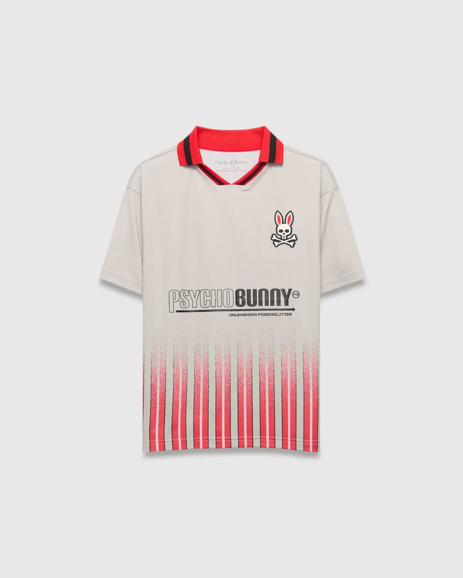 Beige Kids Camden Oversized Soccer Jersey with a red and black striped collar, embroidered Psycho Bunny skull logo on the left chest, large PSYCHO BUNNY graphic, and fading red vertical stripes on the front.