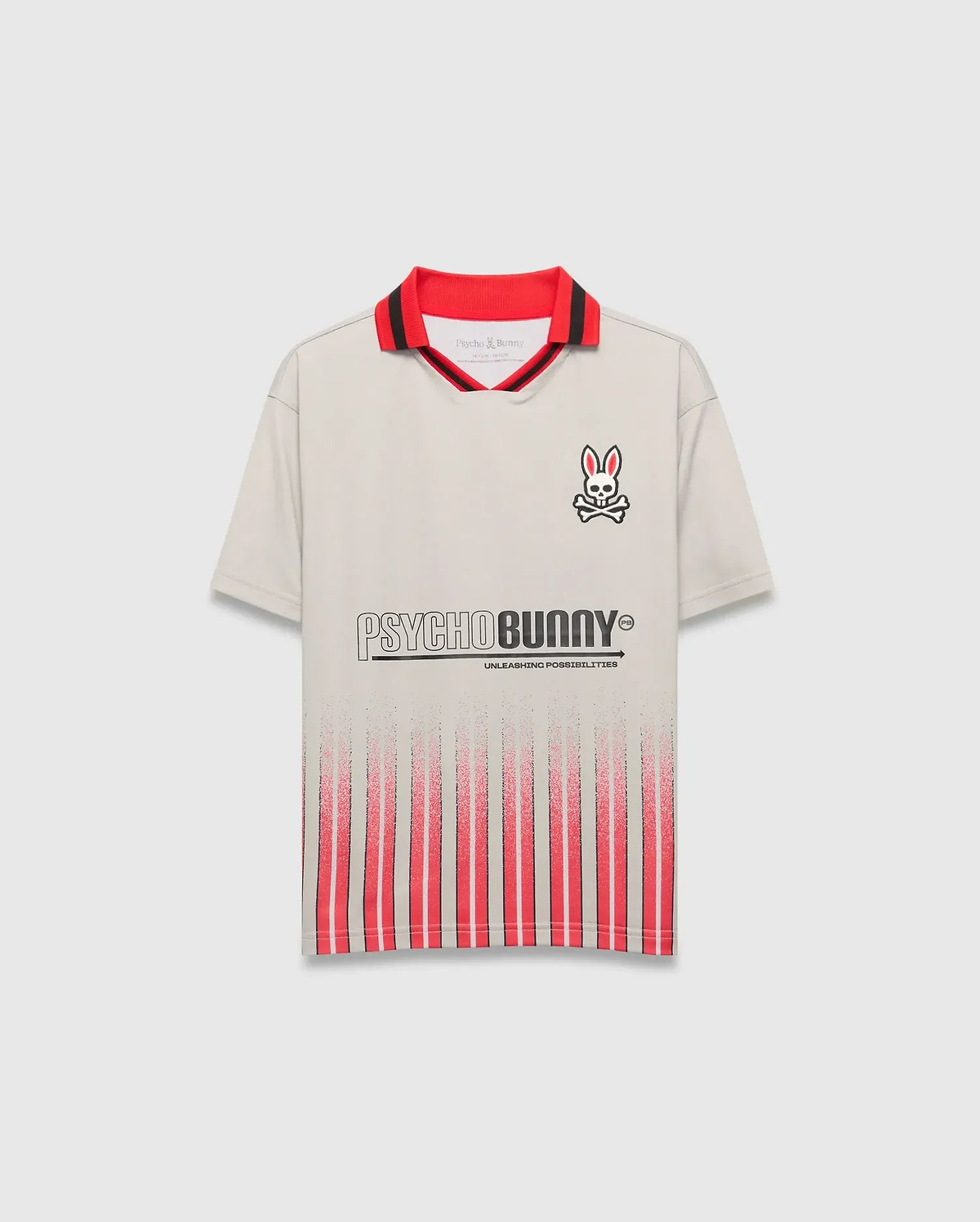 Beige Kids Camden Oversized Soccer Jersey with a red and black striped collar, embroidered Psycho Bunny skull logo on the left chest, large PSYCHO BUNNY graphic, and fading red vertical stripes on the front.