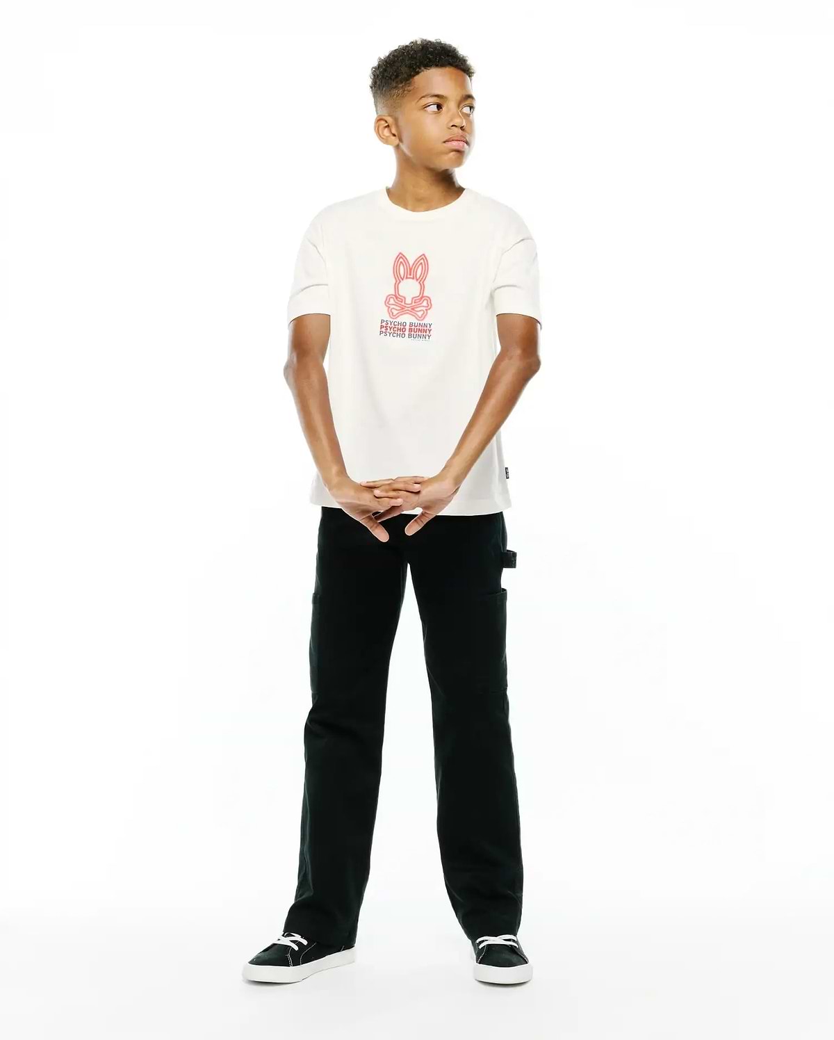 Premium cream jersey Kids Alex Relaxed Back Graphic Tee, featuring a bold red iconic Psycho Bunny skull logo and repeated text graphic on the center chest for refined streetwear style.