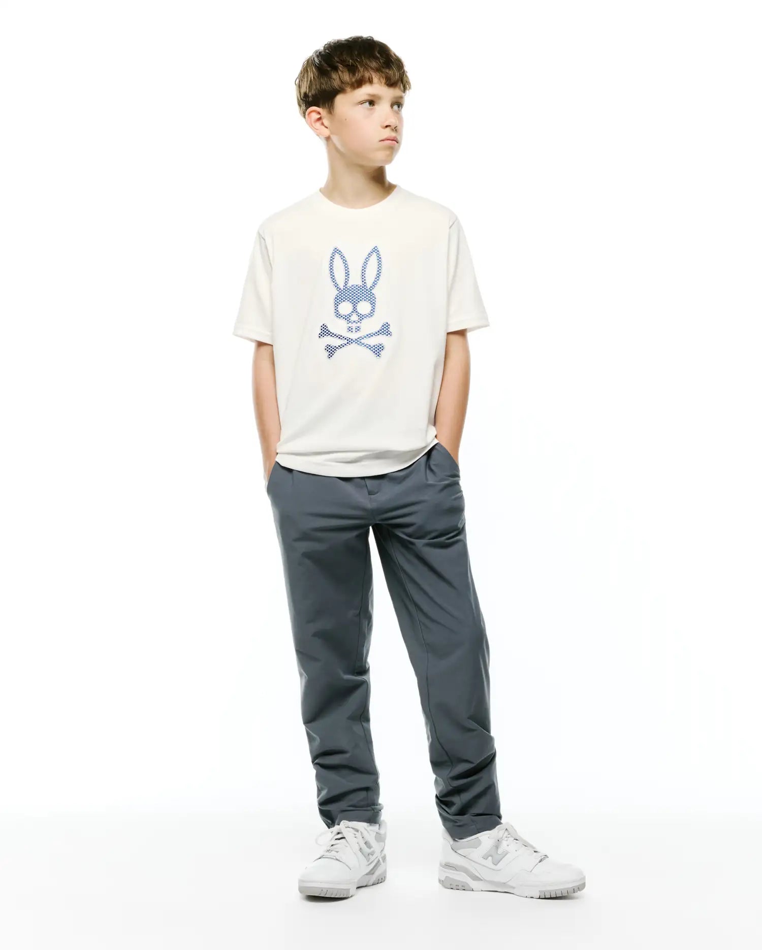 Kids Stan Graphic Tee, an off-white jersey t-shirt with a large blue checkered Psycho Bunny skull and crossbones logo centered on the chest, classic fit.