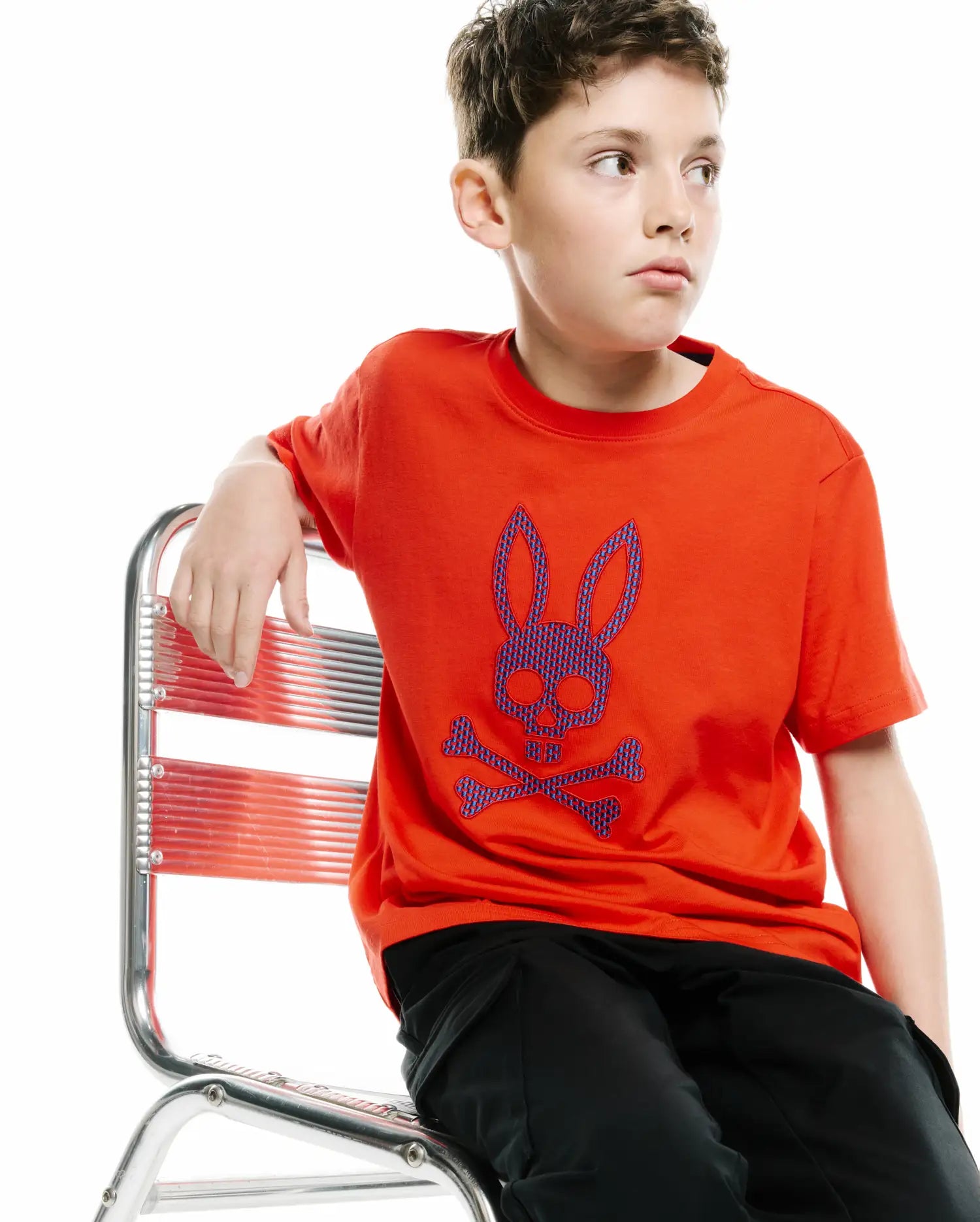 KIDS STAN GRAPHIC TEE in vibrant orange jersey, featuring a large central chest graphic of the iconic Psycho Bunny skull and crossbones logo in blue and purple patterned fill, offering a relaxed fit.