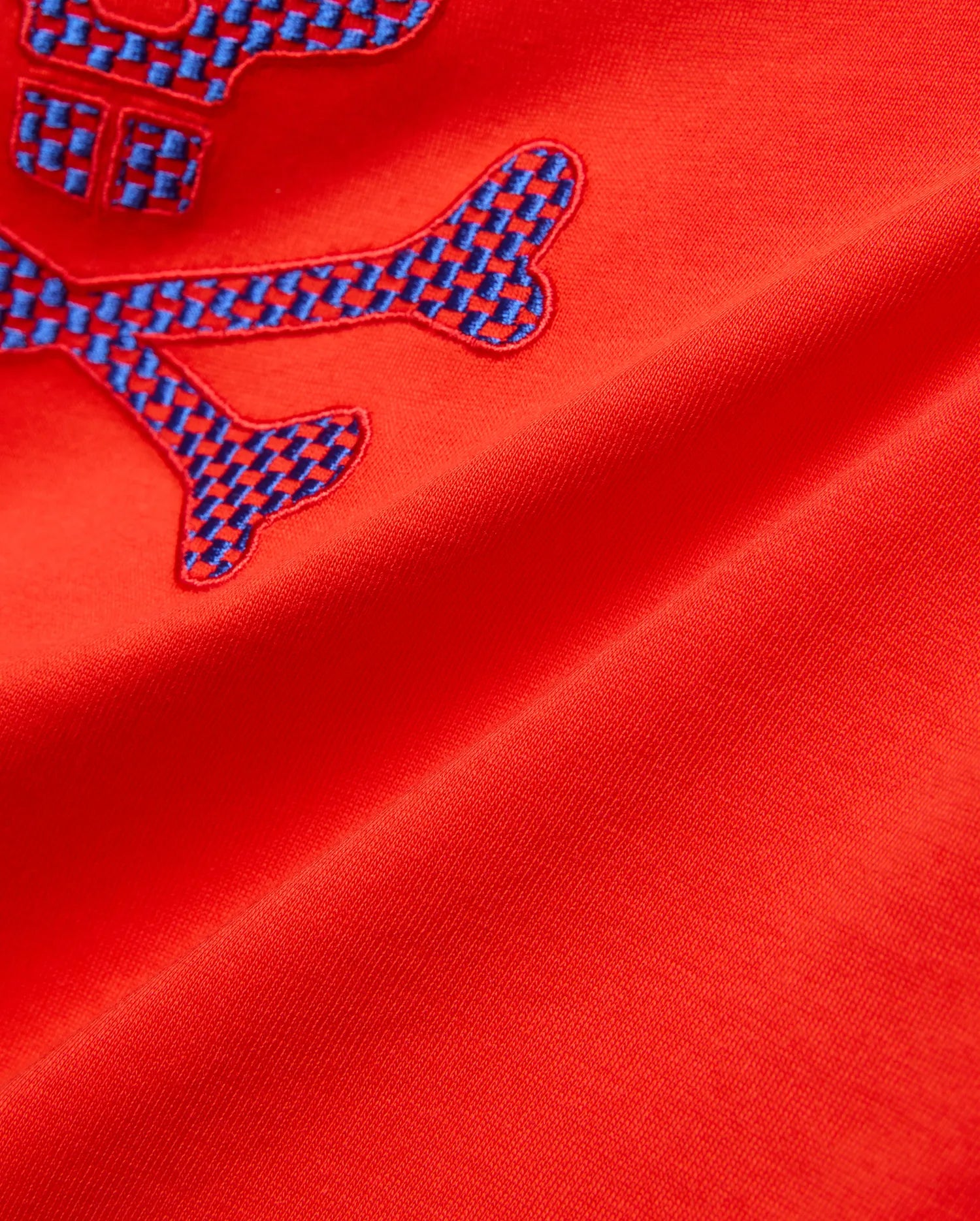 Kids Stan Graphic Tee in bright red jersey knit, showcasing a prominent embroidered Psycho Bunny skull logo with a striking blue checkered pattern.