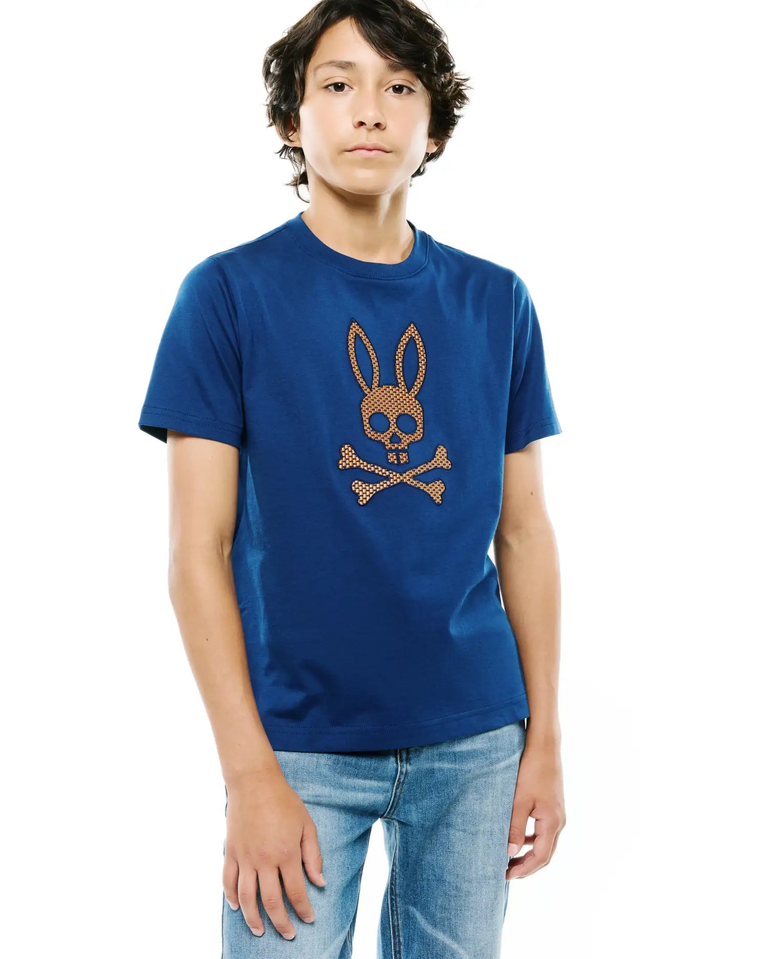 Kids Stan Graphic Tee, a classic fit blue jersey t-shirt featuring a large, textured orange-brown and white Psycho Bunny skull and crossbones logo centered on the chest.