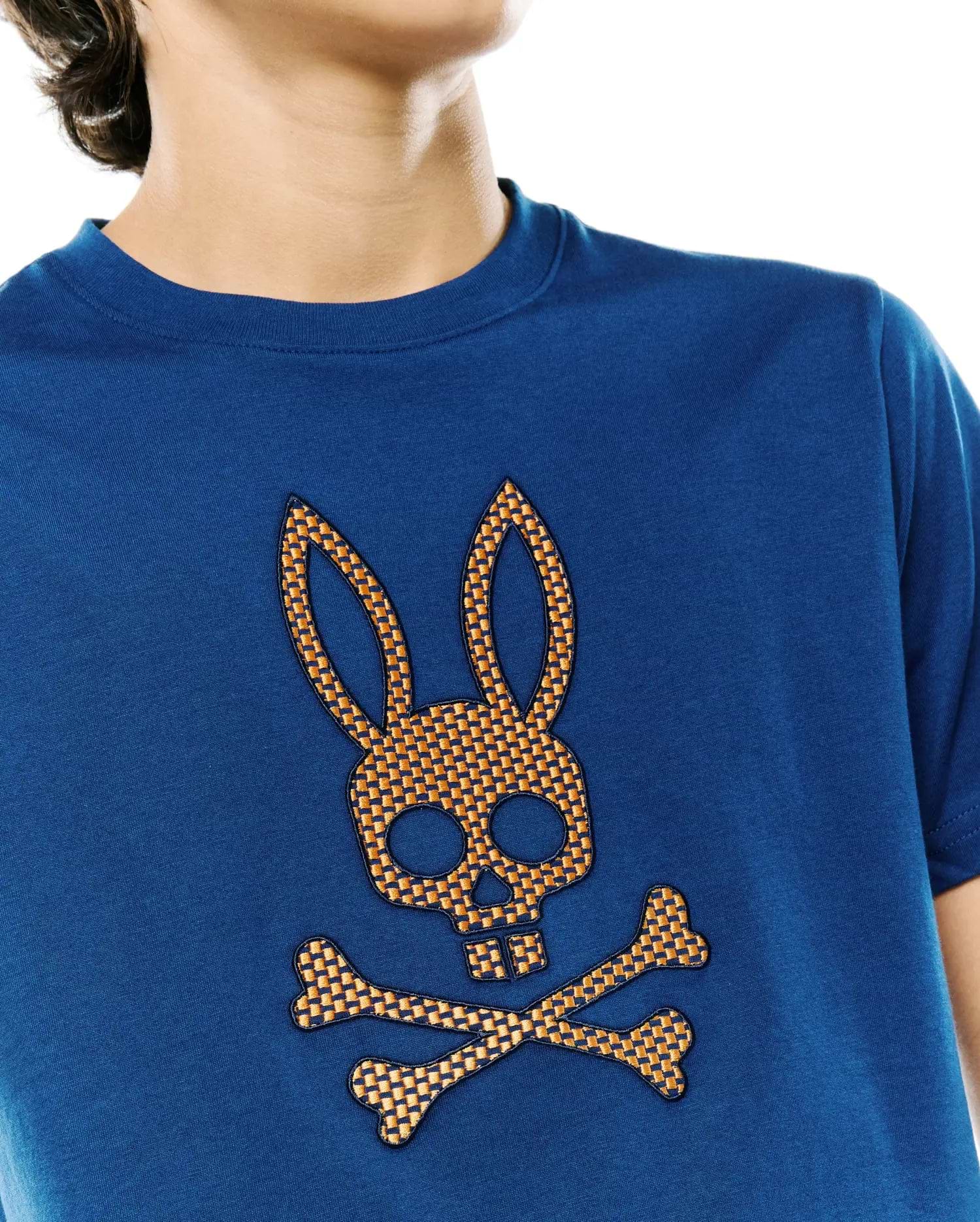 Kids Stan Graphic Tee, a classic fit deep blue jersey t-shirt featuring a prominent, textured orange and black checkered Psycho Bunny skull and crossbones logo on the chest.