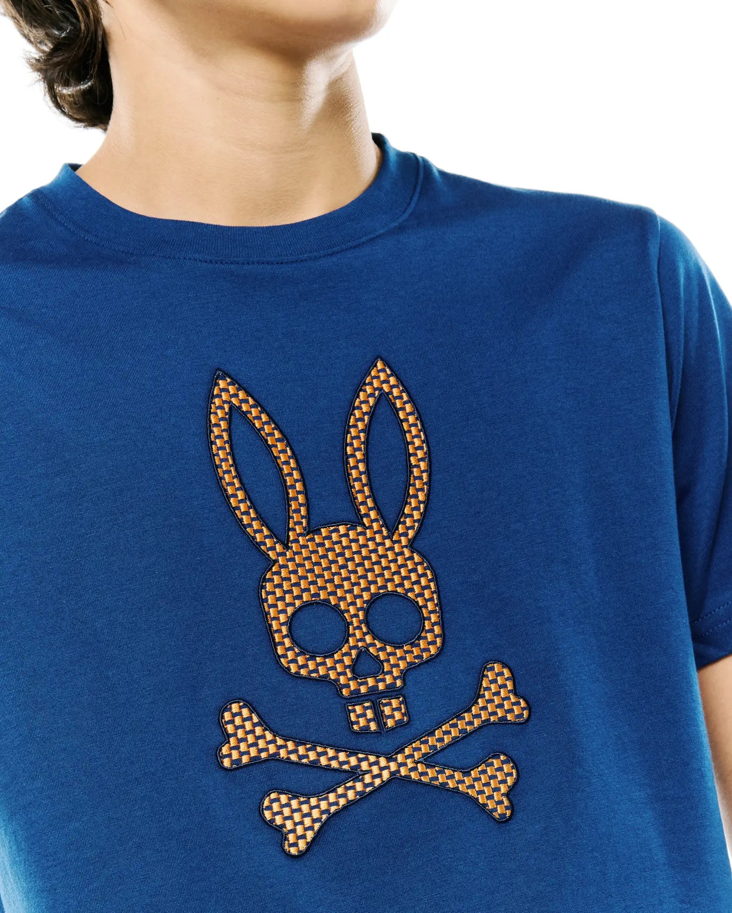 Kids Stan Graphic Tee, a classic fit deep blue jersey t-shirt featuring a prominent, textured orange and black checkered Psycho Bunny skull and crossbones logo on the chest.