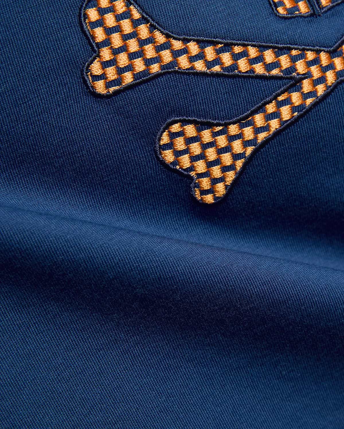 Kids Stan Graphic Tee in navy blue jersey fabric, featuring a large, prominent embroidered Psycho Bunny skull logo with an orange and dark blue checkered pattern.