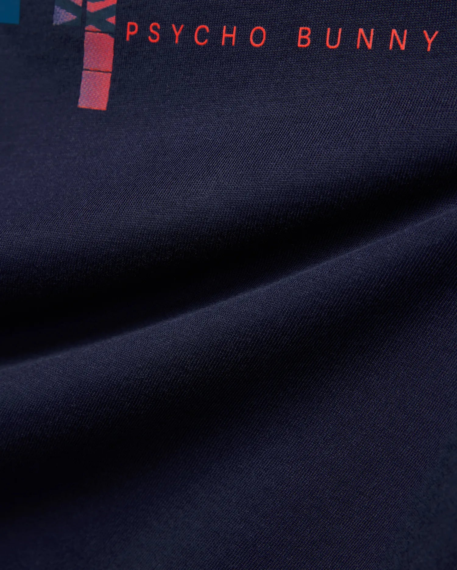 Kids Zander Graphic Tee, a navy jersey knit shirt with a vibrant red PSYCHO BUNNY text print and a modern abstract graphic design featuring red and purple hues.