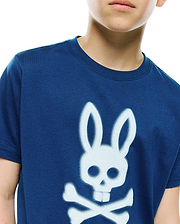 Kids Emmanuel Graphic Tee in navy blue, featuring a classic fit and soft jersey knit. A prominent, large white spray-paint effect Psycho Bunny skull and crossbones graphic adorns the central chest.