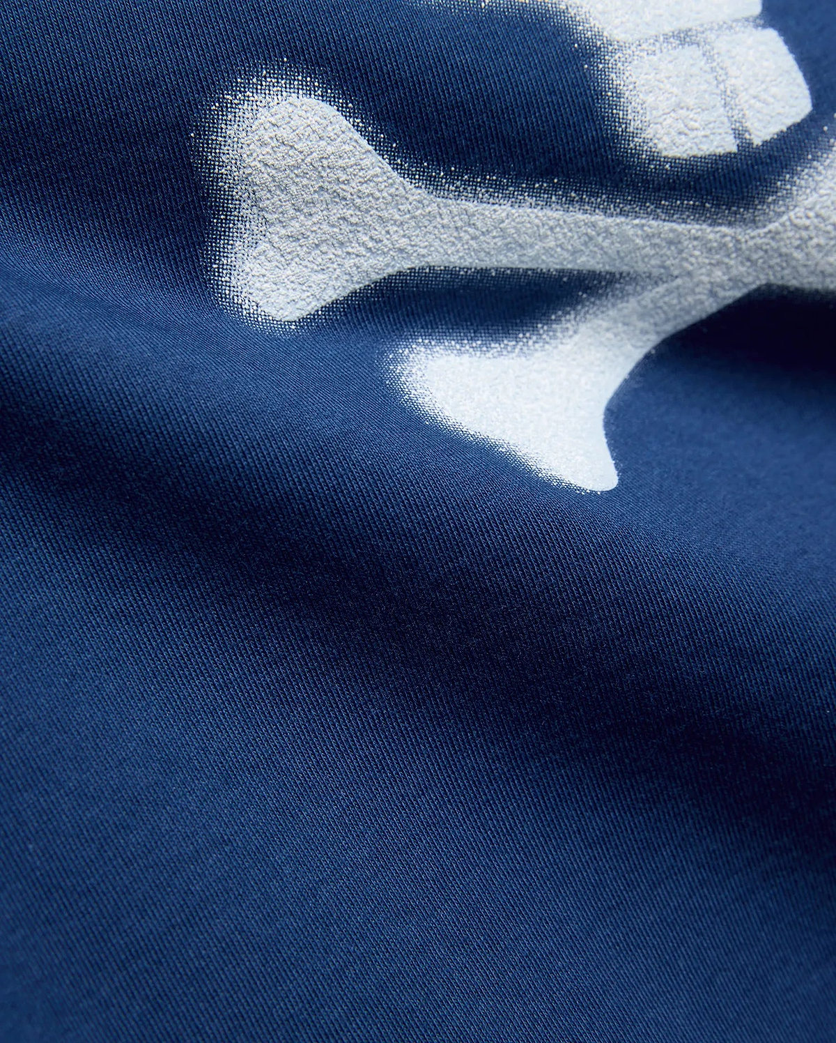 Kids Emmanuel Graphic Tee in deep navy jersey knit, featuring a large, distressed white graphic of a bone, part of the iconic Psycho Bunny skull and crossbones logo.