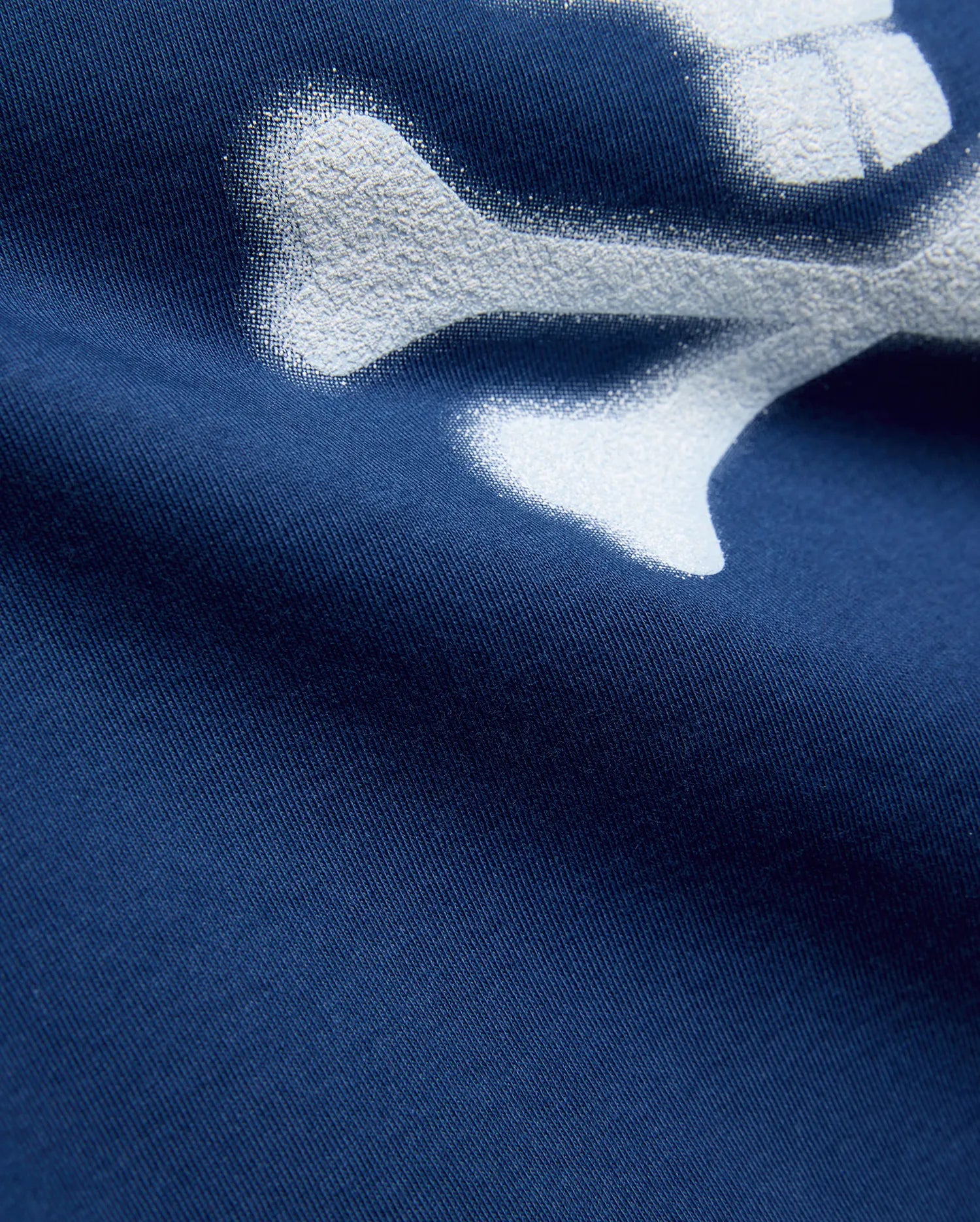 Kids Emmanuel Graphic Tee in deep navy jersey knit, featuring a large, distressed white graphic of a bone, part of the iconic Psycho Bunny skull and crossbones logo.
