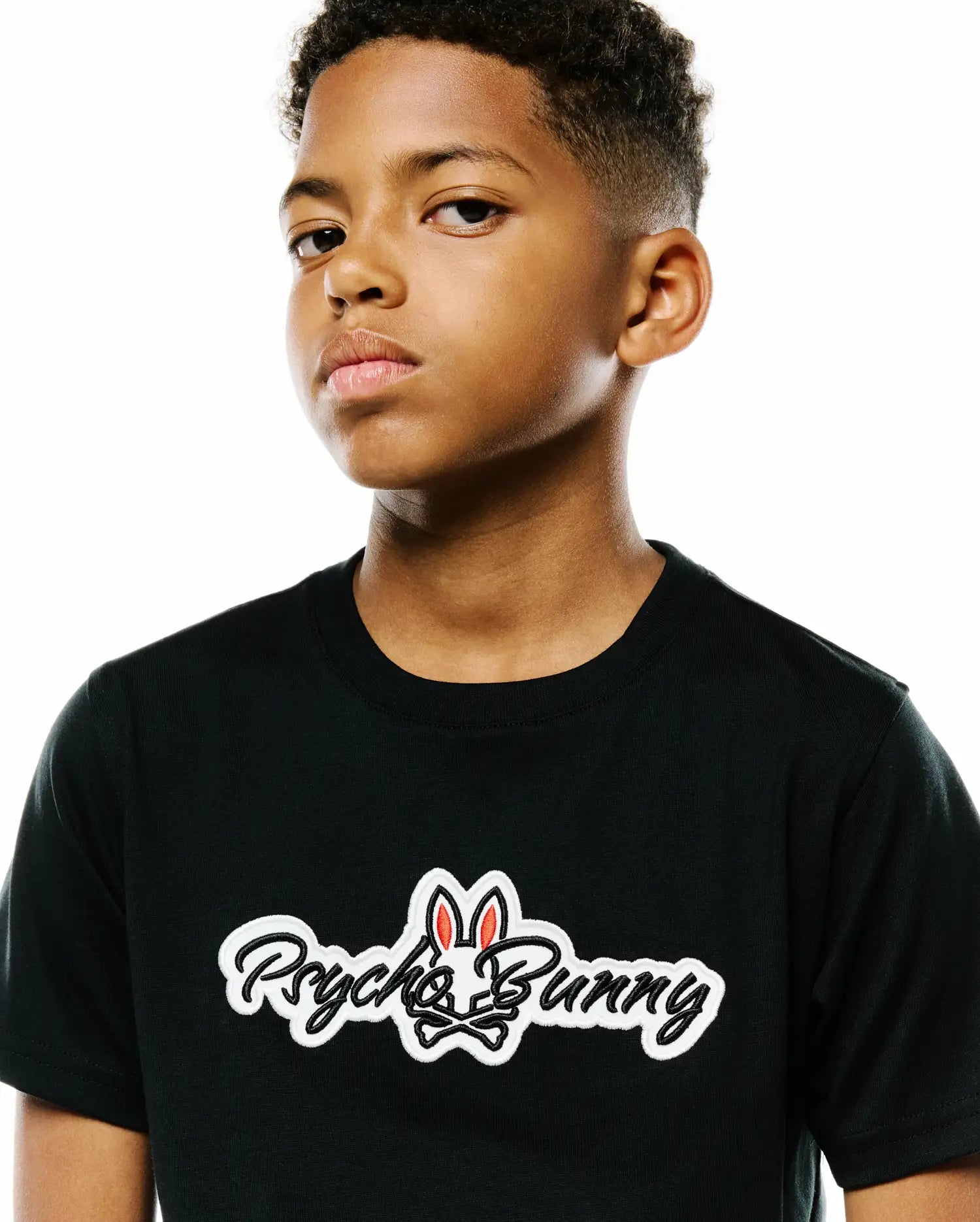 Kids Jaydon Wordmark Graphic Tee, a black classic-fit jersey t-shirt featuring a large embroidered white Psycho Bunny wordmark and skull logo with red ears on the chest.