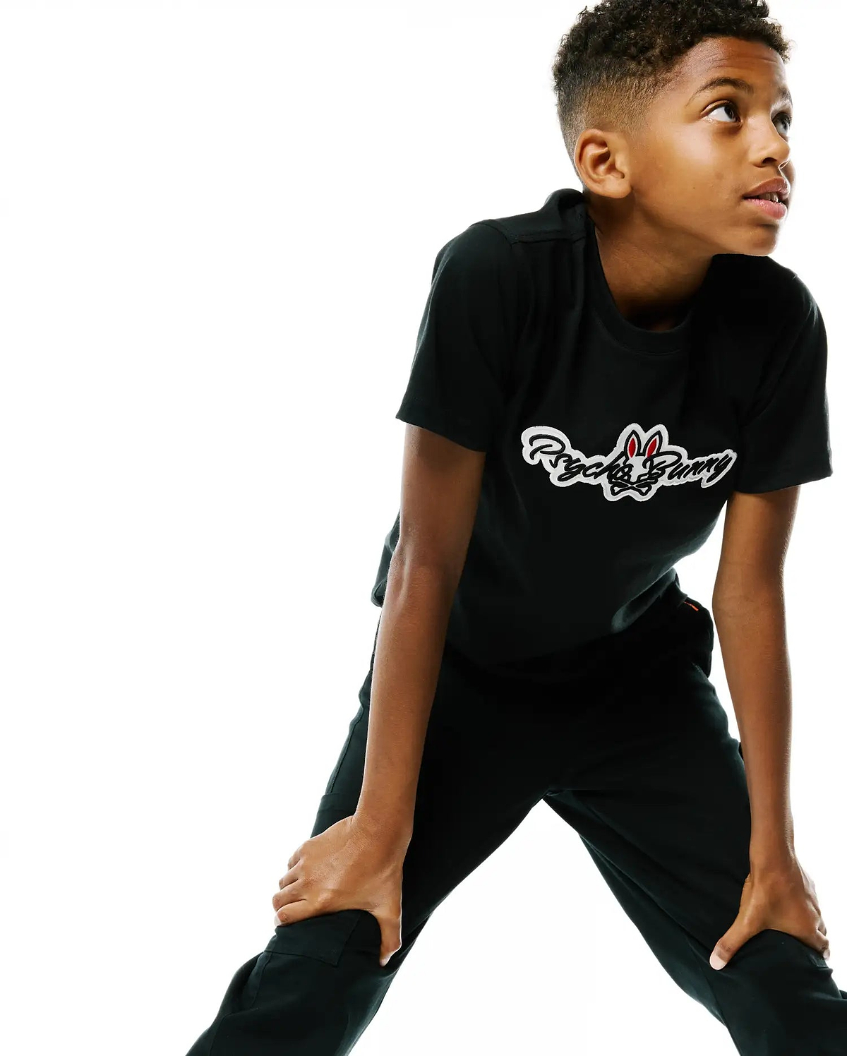 Kids Jaydon Wordmark Graphic Tee in black jersey, featuring a classic fit and a large white Psycho Bunny wordmark graphic with red bunny skull accents on the chest.