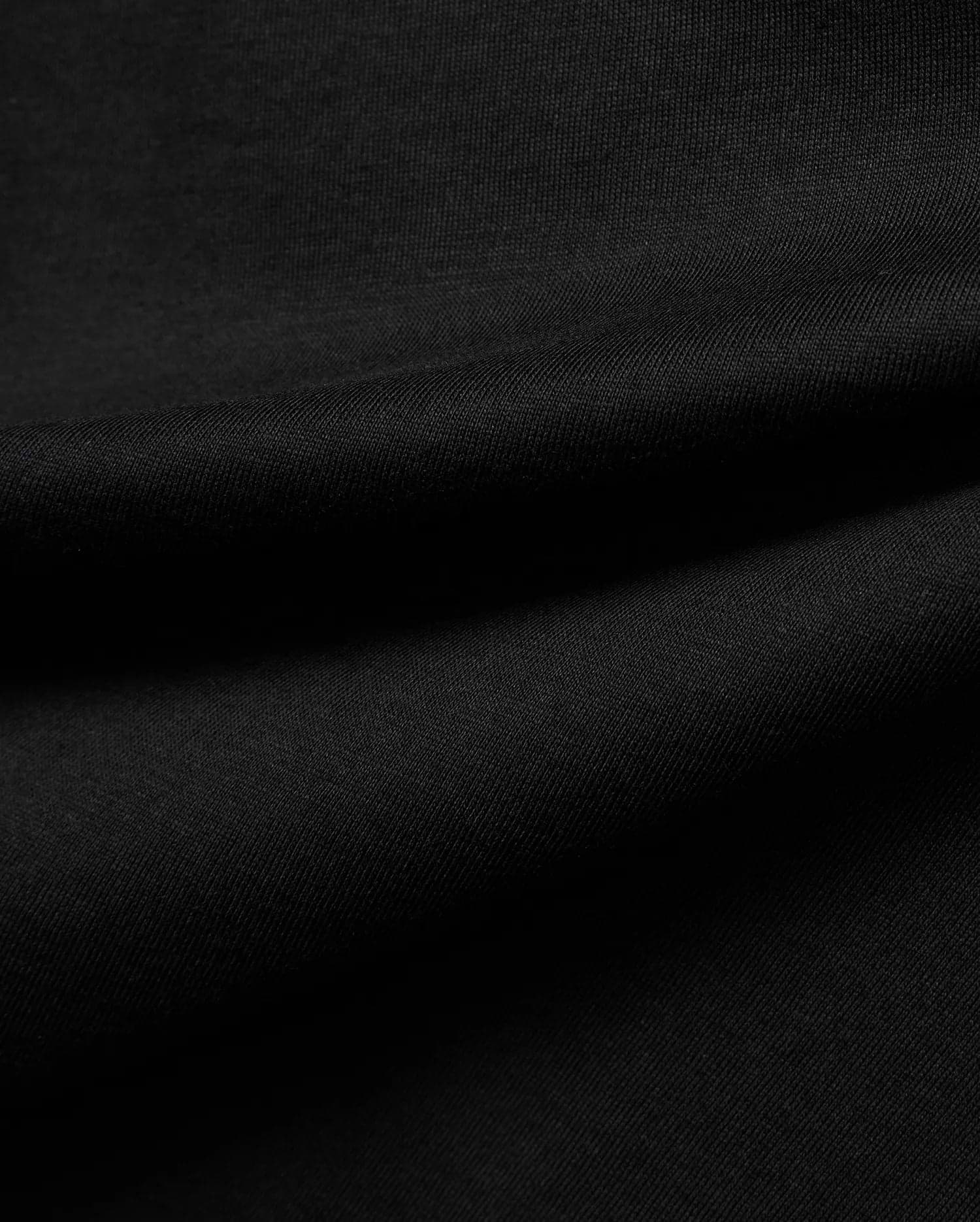Premium black Kids Jaydon Wordmark Graphic Tee fabric, a soft, finely textured jersey knit with visible subtle ribbing and elegant draping folds, highlighting material quality.