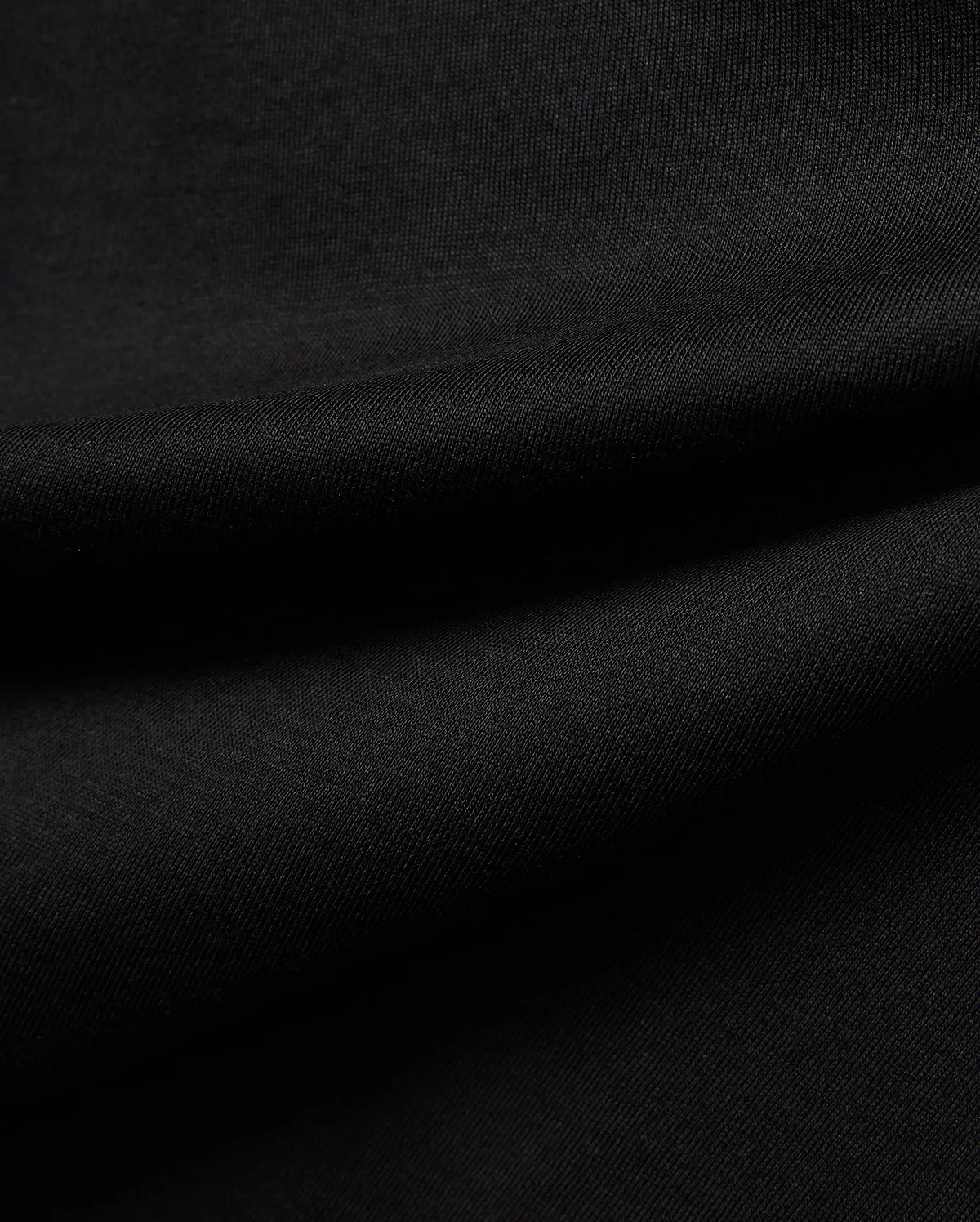 Premium black Kids Jaydon Wordmark Graphic Tee fabric, a soft, finely textured jersey knit with visible subtle ribbing and elegant draping folds, highlighting material quality.