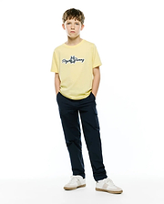 Kids Jaydon Wordmark Graphic Tee, a pale yellow classic fit jersey t-shirt with a medium blue embroidered Psycho Bunny wordmark logo on the center chest, styled with navy cargo pants.