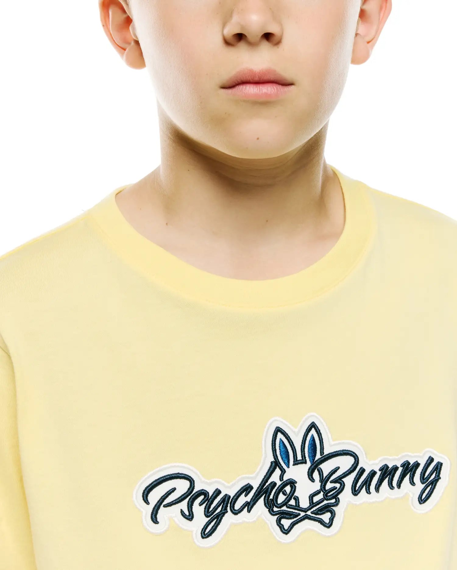 Kids Jaydon Wordmark Graphic Tee in light yellow jersey knit, featuring a large embroidered Psycho Bunny wordmark logo on the chest with a dark blue bunny skull and white outline.